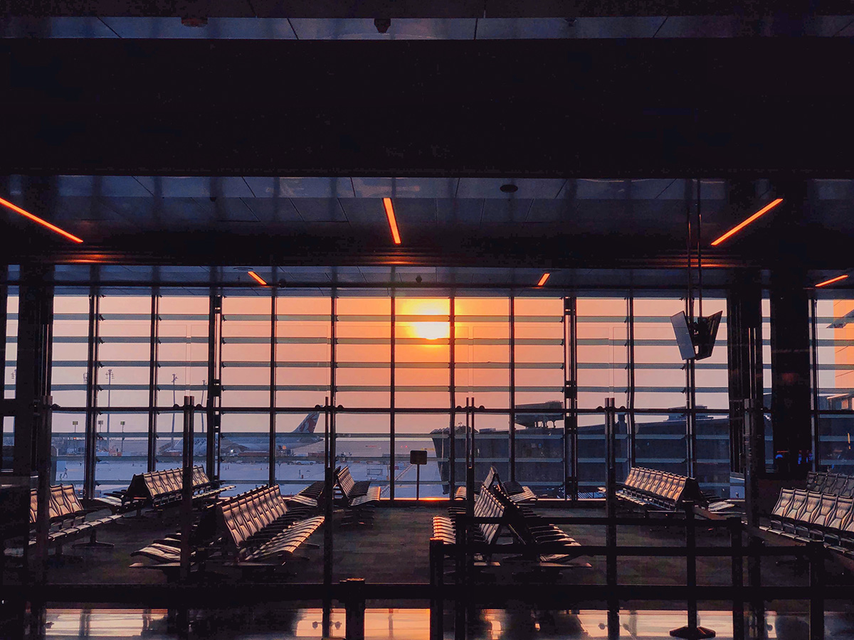 Vacant airport gate area with empty seats and setting sun seen through the large windows.