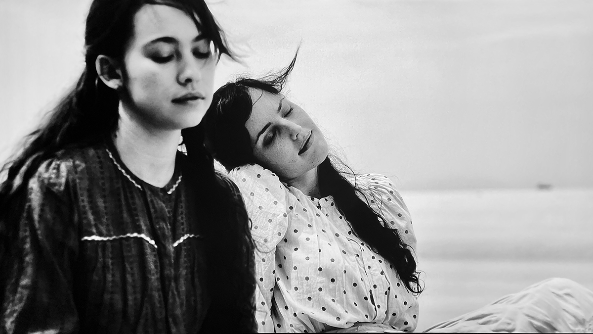 Two young women sitting at the beach, daydreaming